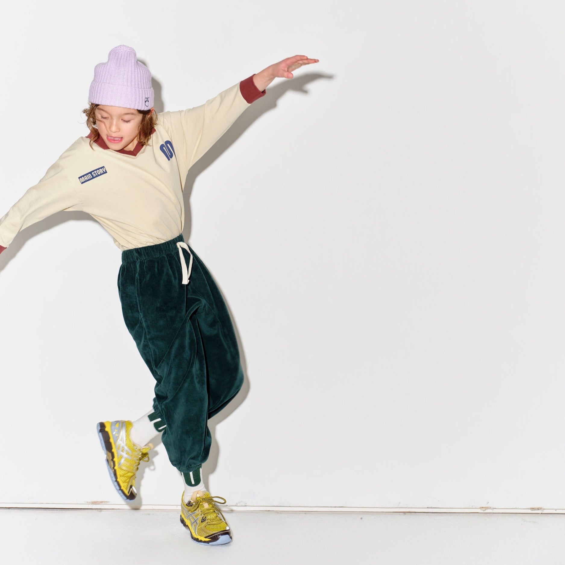 Kid wearing a Main Story beige athletic long sleeve polo tee, green jogger pants, and yellow shoes