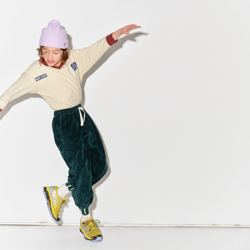Kid wearing a Main Story beige athletic long sleeve polo tee, green jogger pants, and yellow shoes