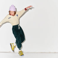 Kid wearing a Main Story beige athletic long sleeve polo tee, green jogger pants, and yellow shoes