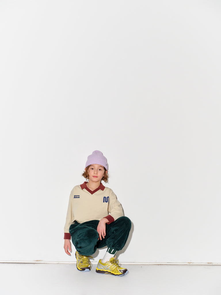 Kid wearing a Main Story beige athletic long sleeve polo tee, green jogger pants, and yellow shoes