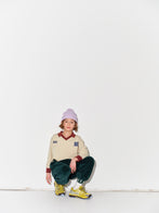 Kid wearing a Main Story beige athletic long sleeve polo tee, green jogger pants, and yellow shoes