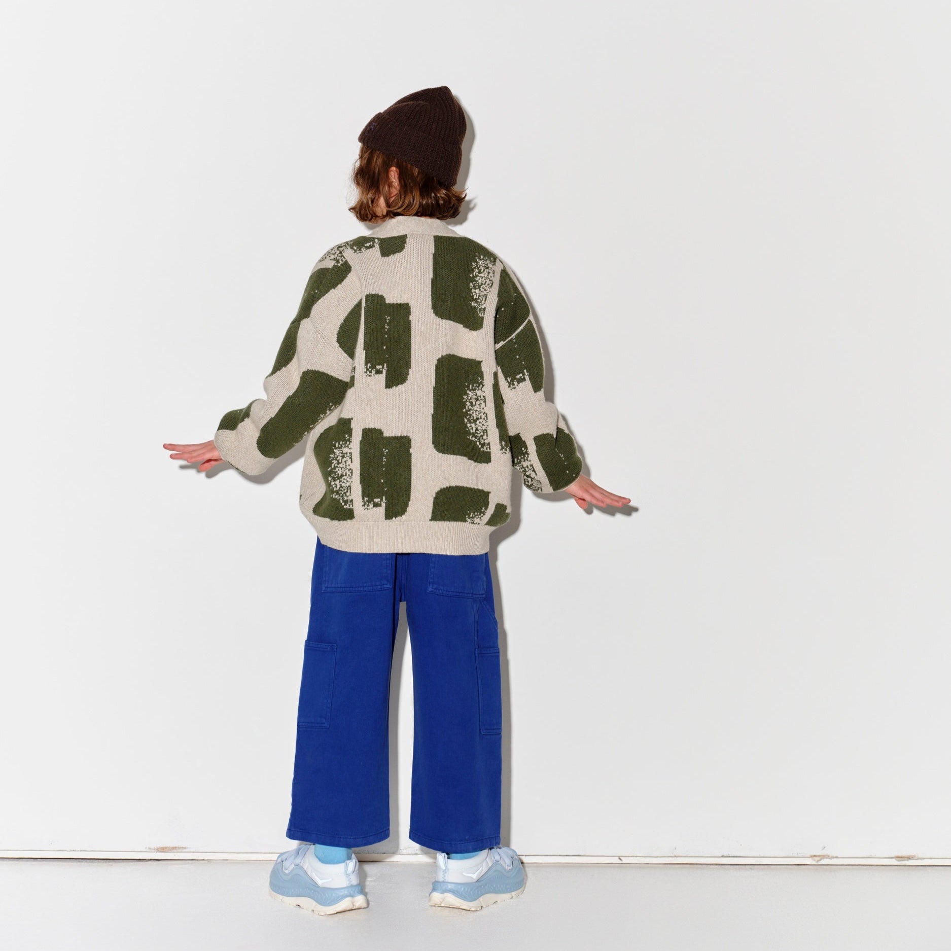 Kid wearing a Main Story patterned sweater and blue painter cargo pants with dark brown knit beanie