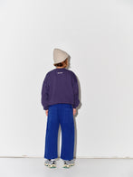 Child wearing a Main Story beige knit beanie, purple sweatshirt with a graphic design, true blue painter cargo pants, and sneakers