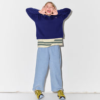 Person wearing a Main Story blue sweatshirt, striped t-shirt, and light dusty blue corduroy lounge pants with yellow sneakers