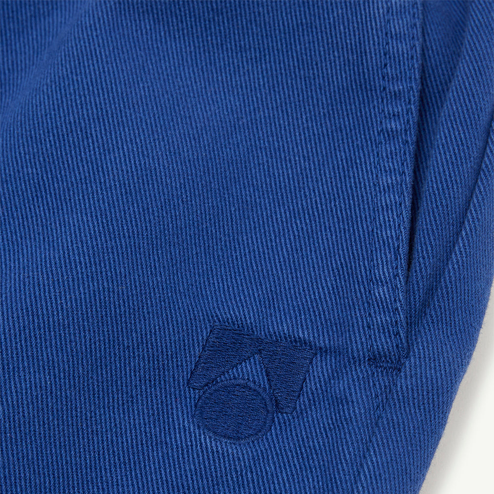 Close-up of True Blue organic cotton twill fabric with a tonal embroidered  logo on a white background