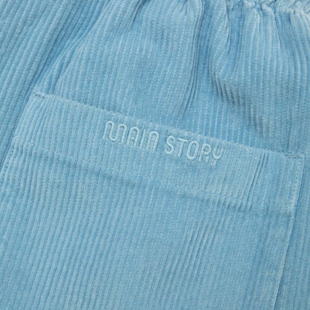 Close up of light dusty blue corduroy pants with 'MAIN STORY' branding on pocket