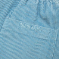 Close up of light dusty blue corduroy pants with 'MAIN STORY' branding on pocket