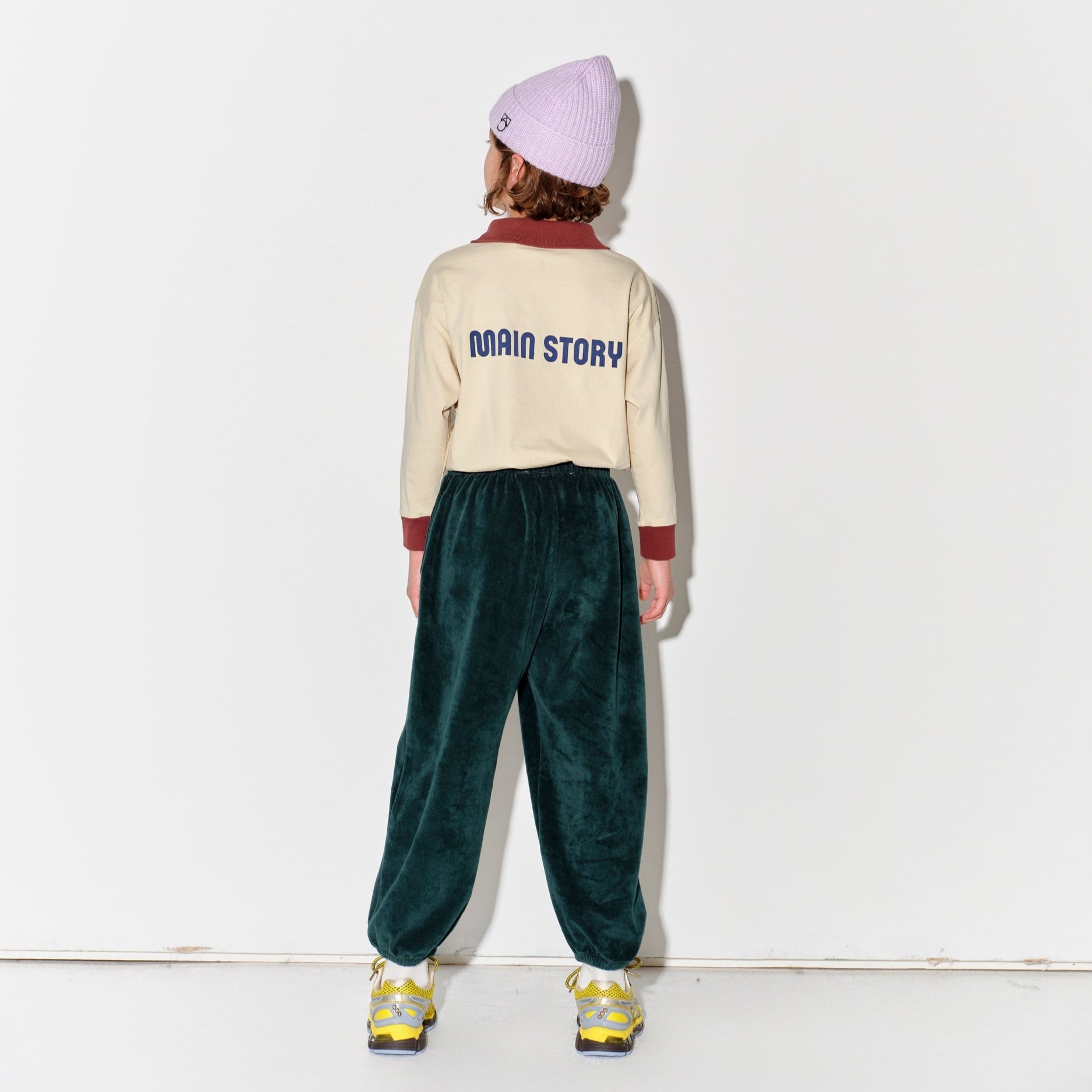 Kid wearing a Main Story beige athletic long sleeve polo tee, green jogger pants, and yellow shoes