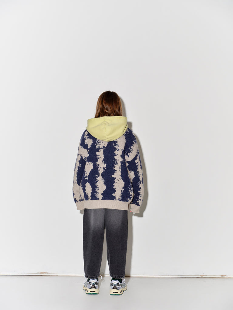 Child wearing a patterned Main Story knit cardigan over a yellow shirt with faded baggy black jeans