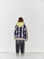 Child wearing a patterned Main Story knit cardigan over a yellow shirt with faded baggy black jeans