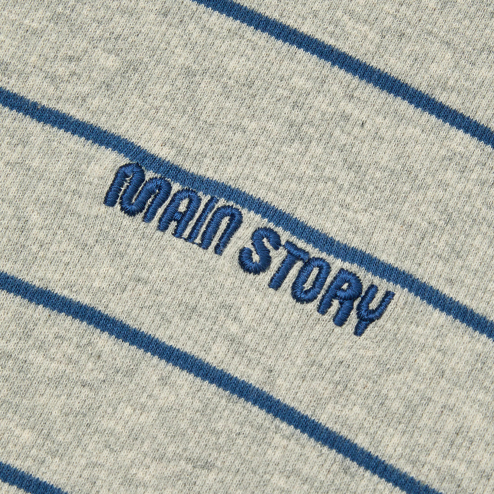 Close-up of a Main Story Rolled Neck melange gray organic cotton fabric with  blue stripes and 'MAIN STORY' embroidered in blue thread.