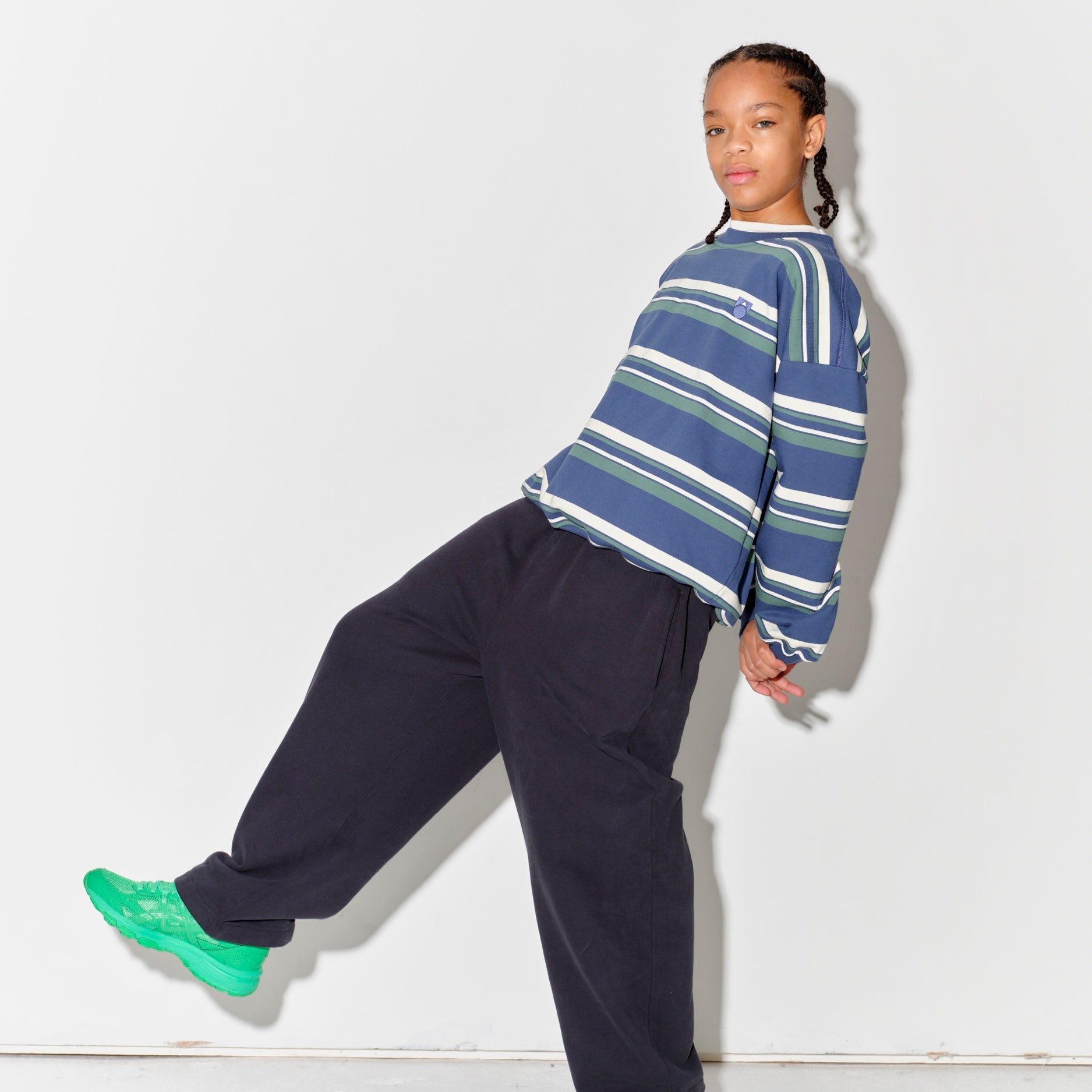 Child wearing a Main Story blue striped sweatshurt and dark grey lounge pants with green shoes