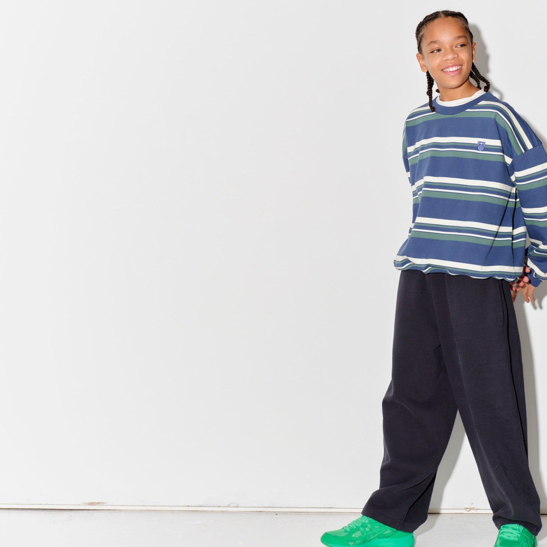 Child wearing a Main Story blue striped sweatshurt and dark grey lounge pants with green shoes