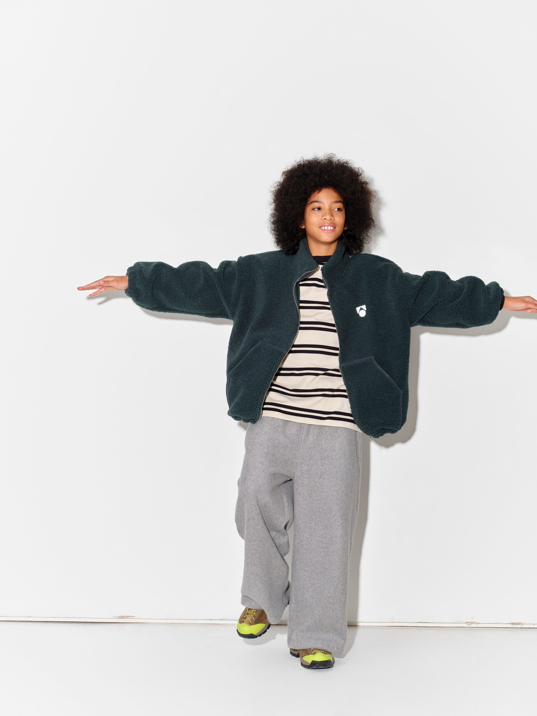 Child wearing a Main Story bottle green teddy fleece jacket, striped tshirt, and gray sweatpants