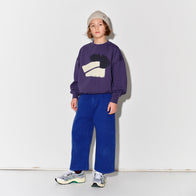 Child wearing a Main Story beige knit beanie, purple sweatshirt with a graphic design, and true blue painter cargo pants
