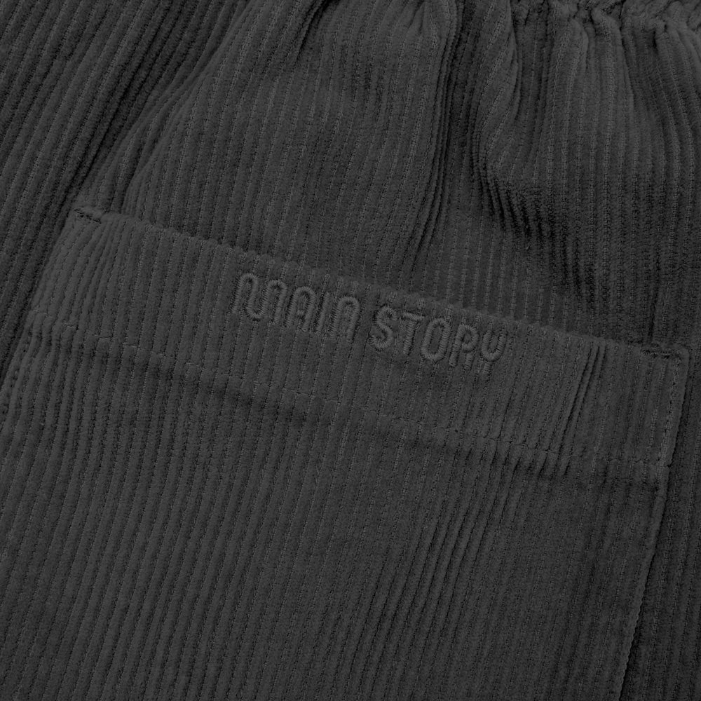 Close-up of dark gray corduroy pants with 'Main Story' branding on a matching fabric.