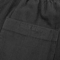 Close-up of dark gray corduroy pants with 'Main Story' branding on a matching fabric.